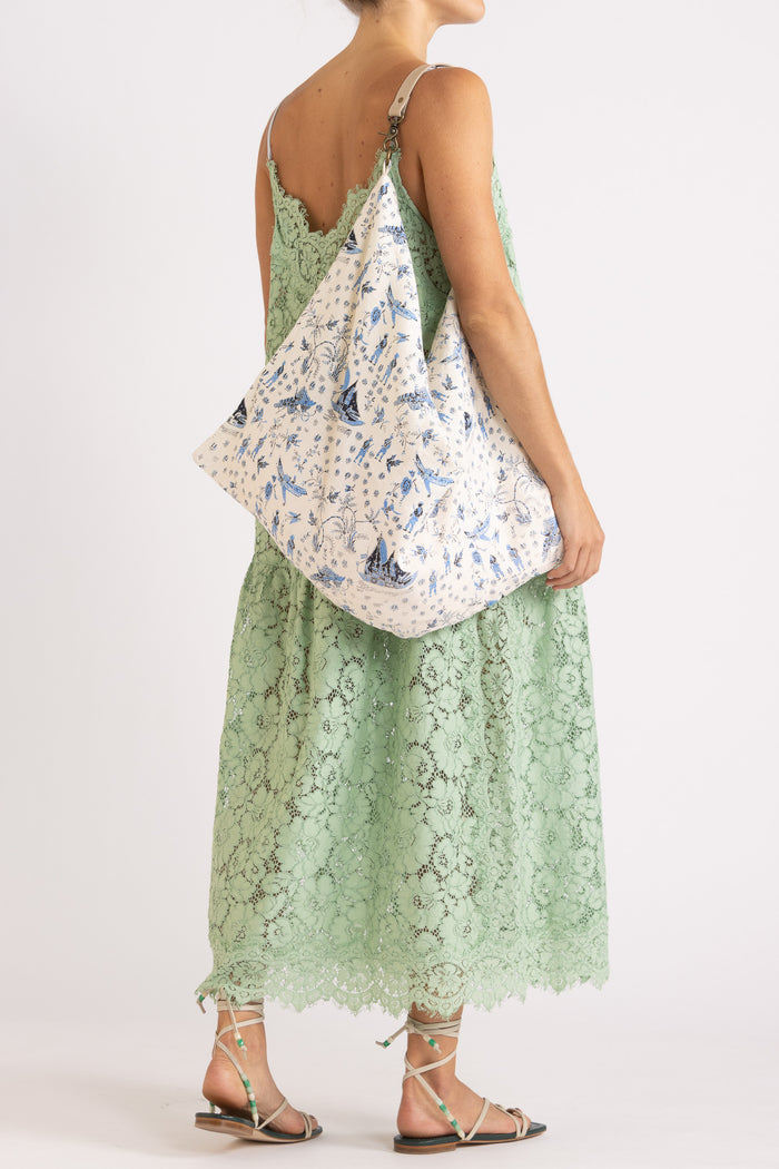 Woman wearing an apple floral lace maxi dress with a cream tote bag with features a blue limited edition percussion print