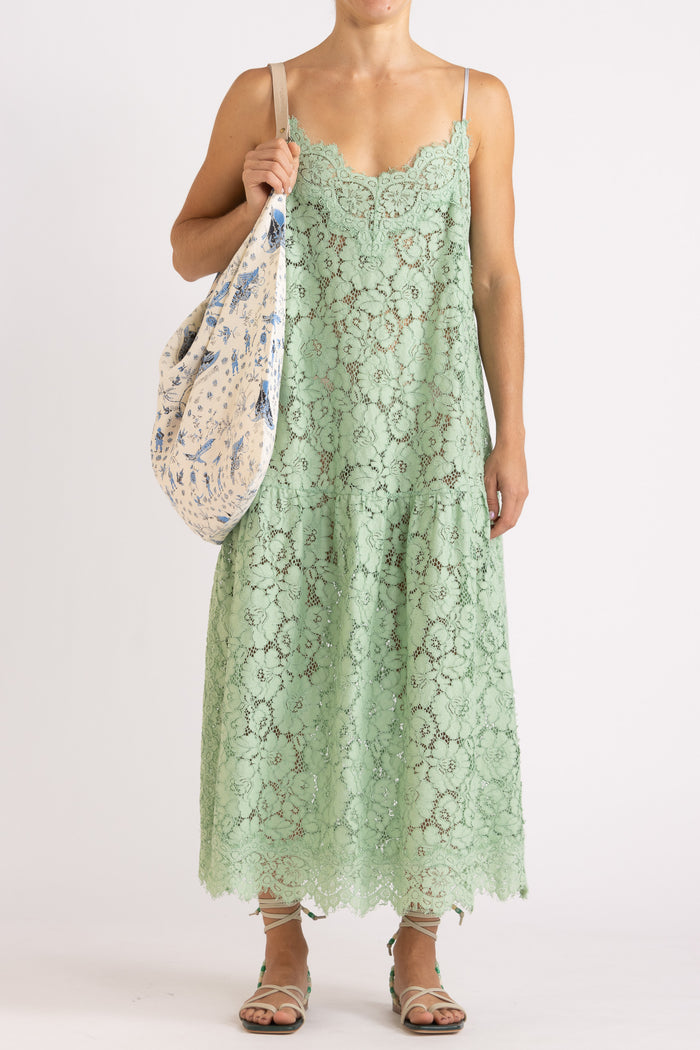 Woman wearing an apple floral lace maxi dress with a cream tote bag with features a blue limited edition percussion print