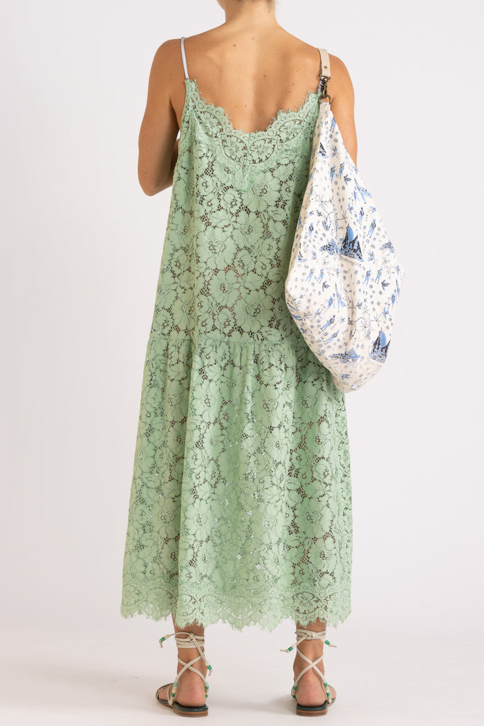 Woman wearing an apple floral lace maxi dress with a cream tote bag with features a blue limited edition percussion print