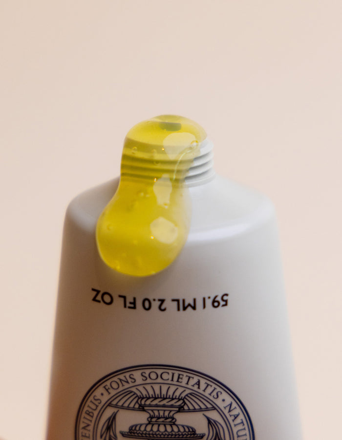 A close-up of the Cozy Earth Enzyme Mask: a white tube with black text and a circular emblem near the bottom, dispensing yellow gel. The softly lit background is plain.|Size:Full Size