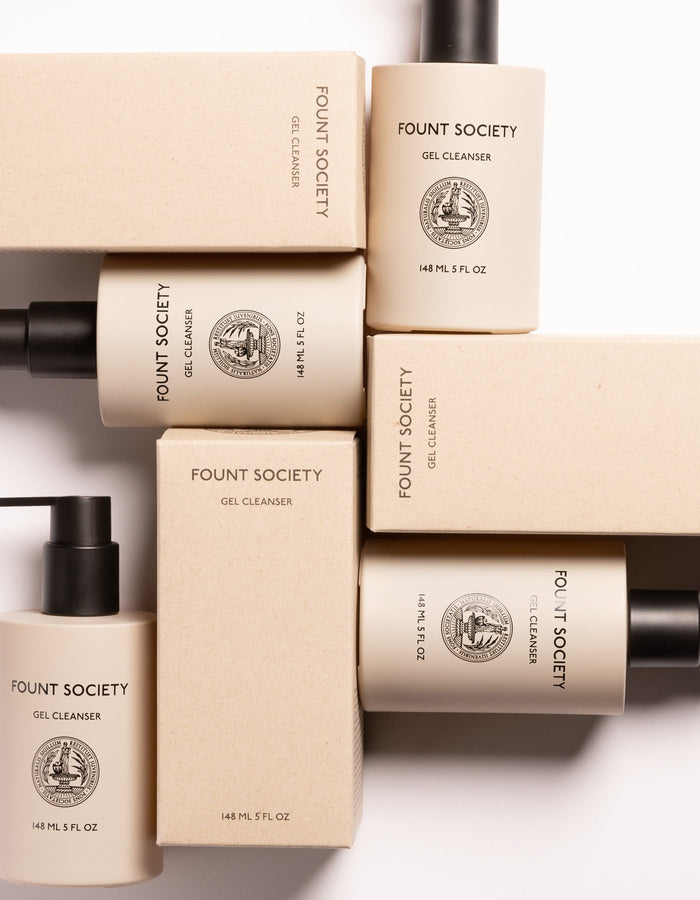 A flat lay of Cozy Earth Gel Cleanser bottles and their beige packaging boxes arranged in a neat, geometric pattern. The cylindrical bottles have black pumps and white labels with black text, stating the product details and volume (148ml/5 fl oz).|Size:Full Size