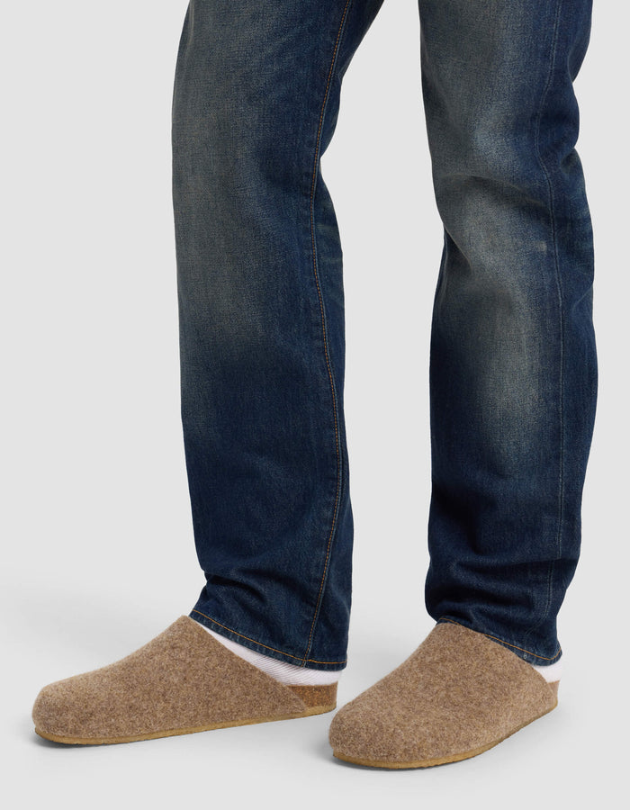 A person wearing blue jeans and Cozy Earth's Lakehouse Clog in tan stands on a light gray background, with only their lower legs and feet visible.|Color:Chestnut