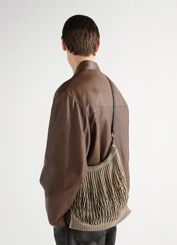 Large beige macramé crossbody bag with black strap worn by model in brown leather jacket LEMAIRE back view