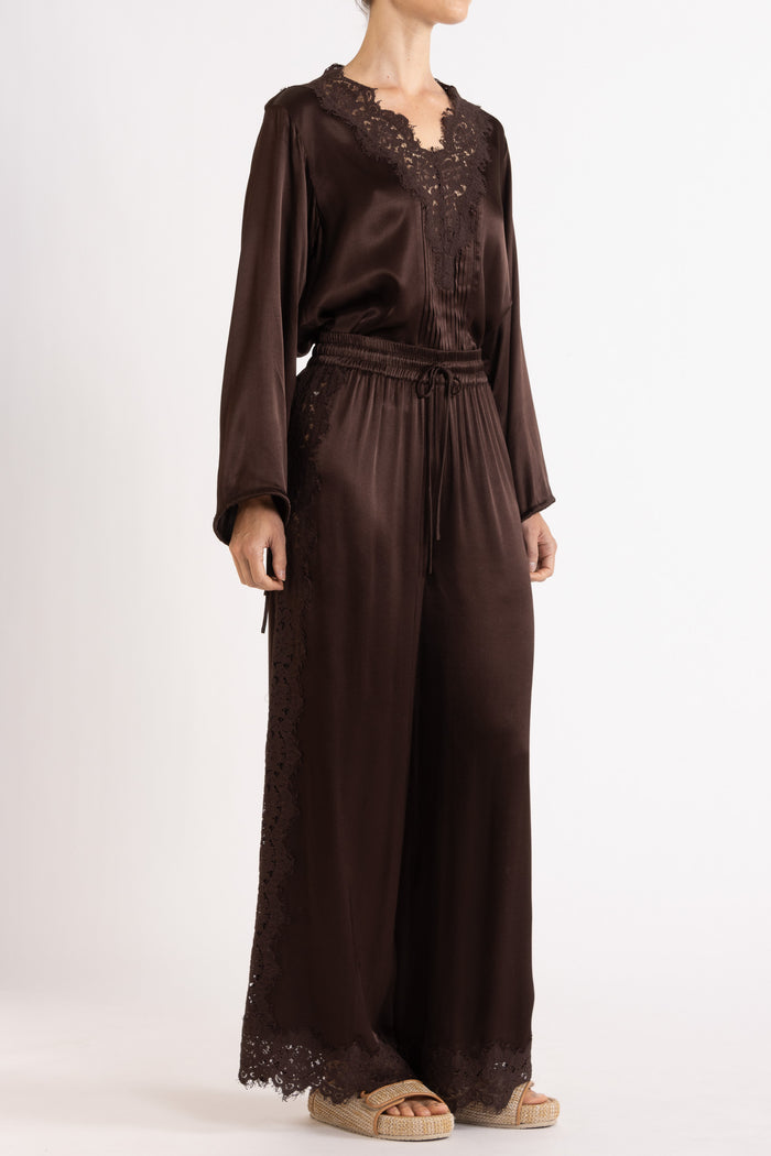 Woman wearing a brown long sleeve top and pant with lace details on a white background