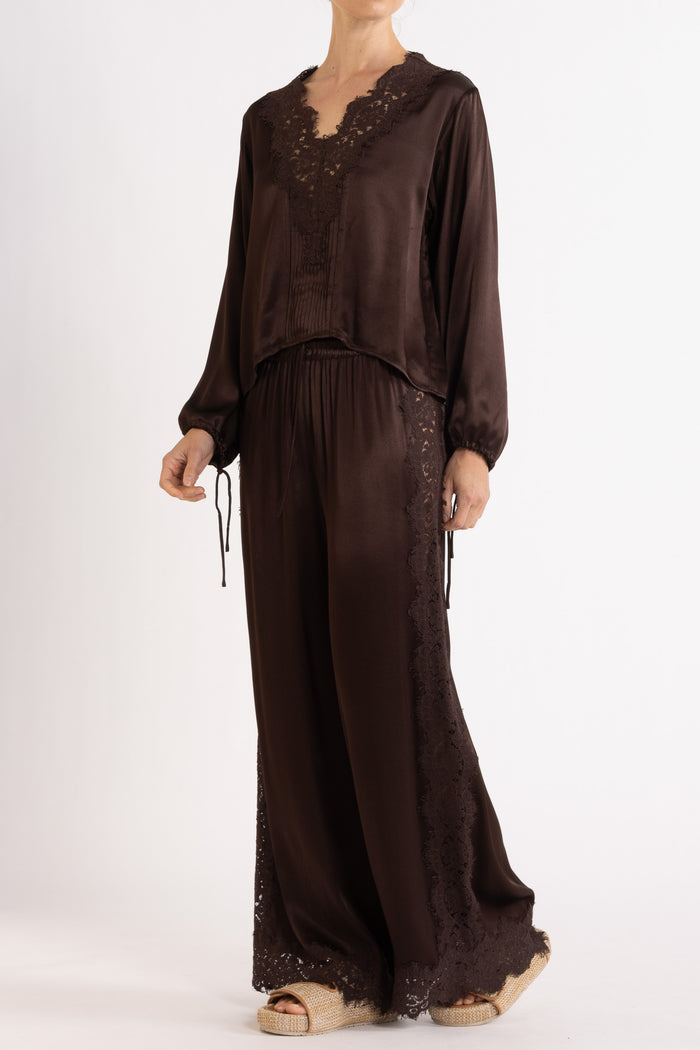 Woman wearing a brown long sleeve top and pant with lace details on a white background