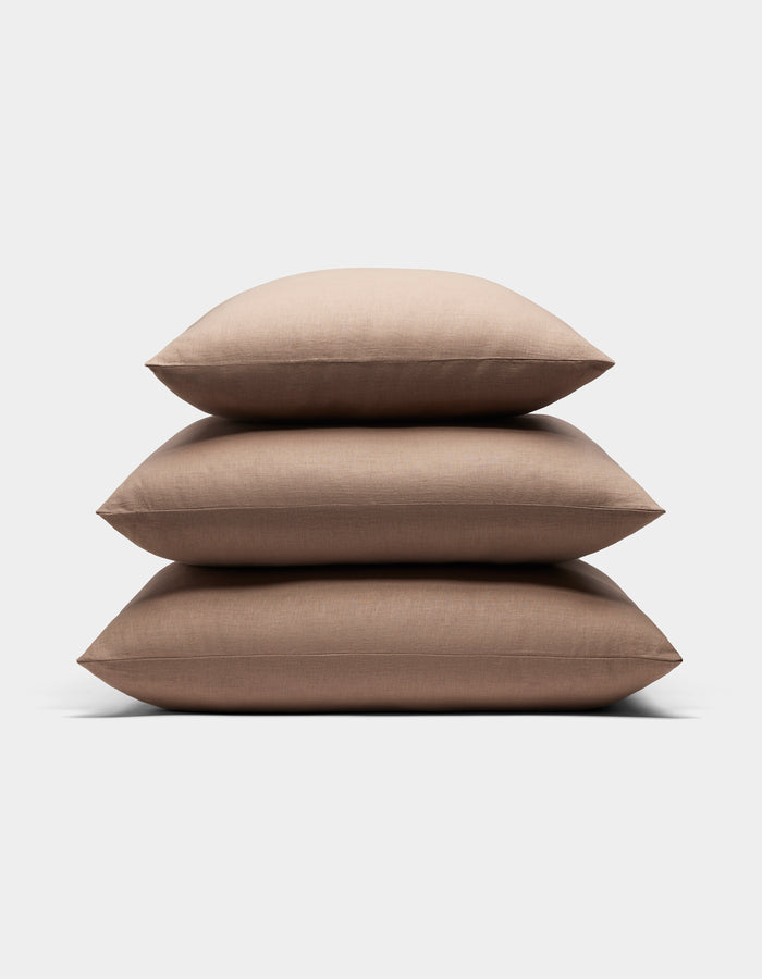 Three Cozy Earth Linen Throw Pillows in light brown are stacked neatly on top of each other against a plain white background.|Color:Maple|Size:24" x 24"