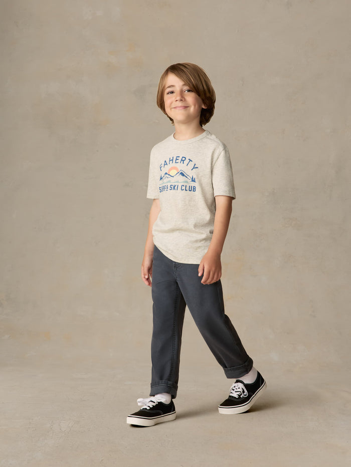 Child wearing a grey surf & ski club tee and black pants against a beige background