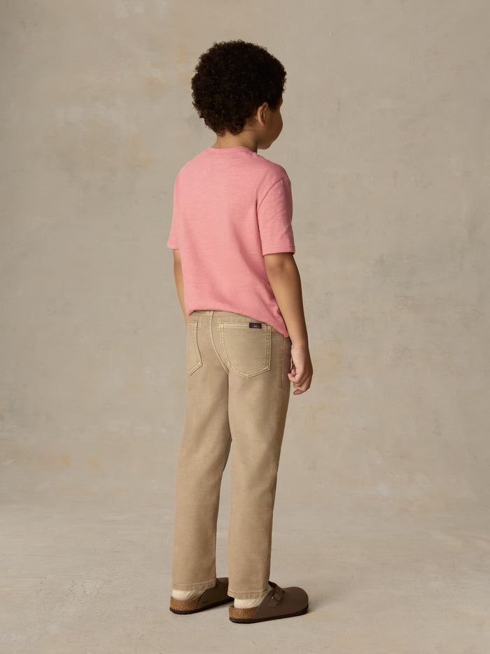 Child wearing a red t-shirt and beige pants against a beige background