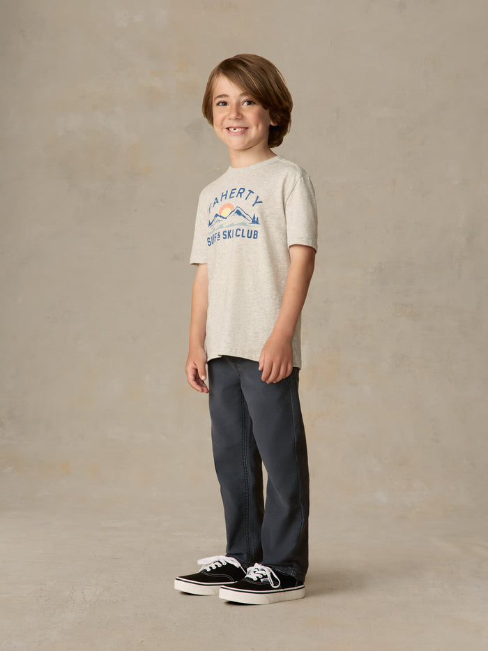 Child wearing graphic grey tee and navy pants against a beige background