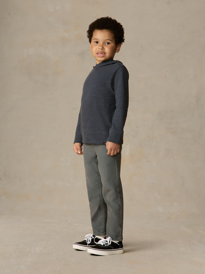 Child wearing blue hoodie and grey pants against a beige background