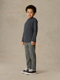 Child wearing blue hoodie and grey pants against a beige background