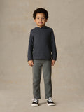 Child wearing a navy hoodie and grey pants against a beige background