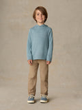 Child wearing a light blue hoodie and beige pants against a beige background