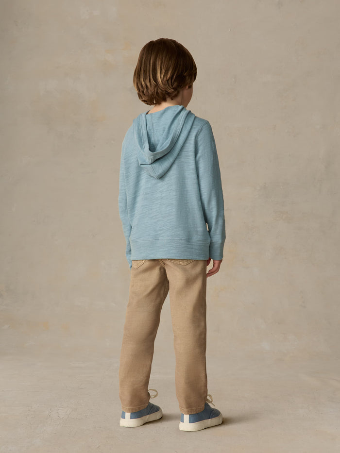 Child wearing a light blue hoodie and beige pants against a beige background
