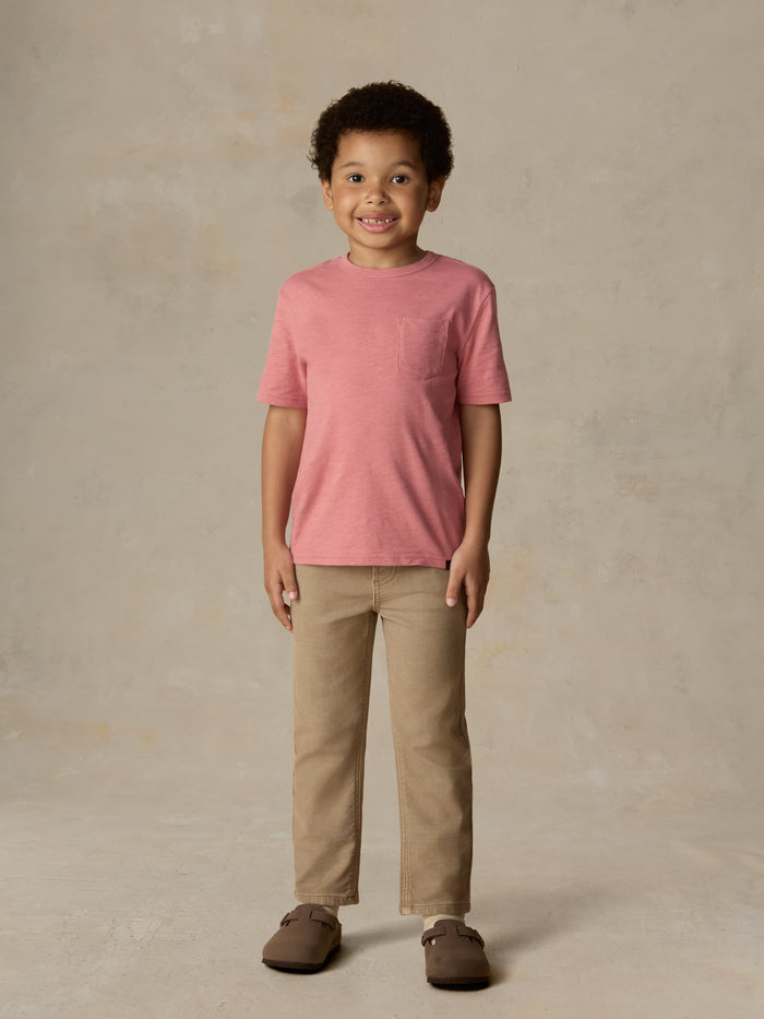 Child wearing a red pocket tee and beige pants against a beige background