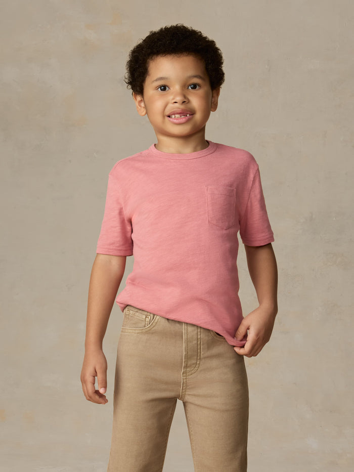 Child wearing a red pocket tee and beige pants against a beige background