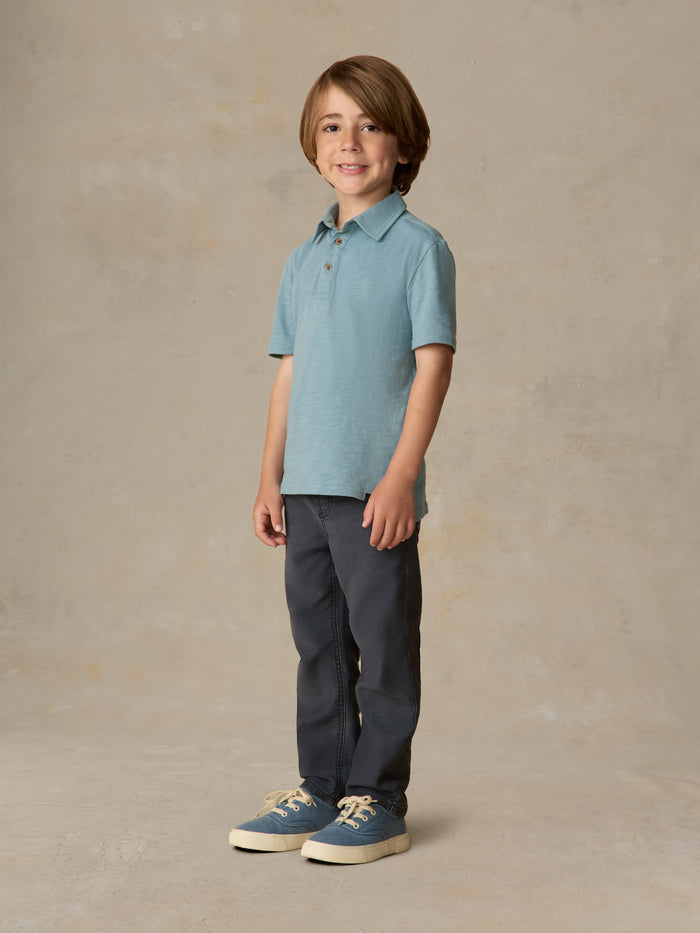 Child wearing a light blue polo shirt and navy pants against a beige background