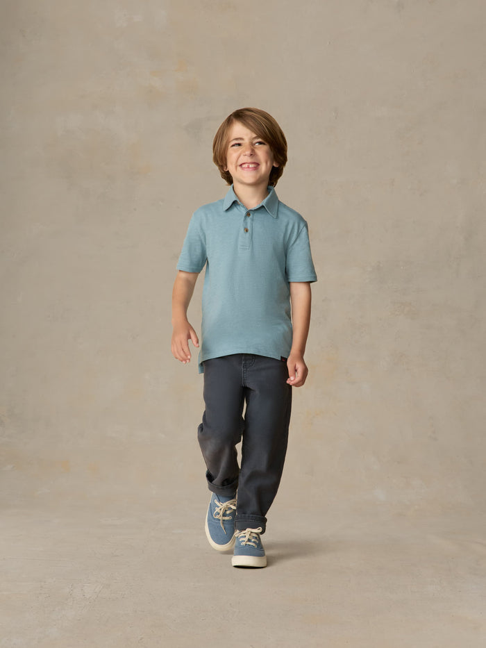Child wearing a light blue polo shirt and navy pants against a beige background