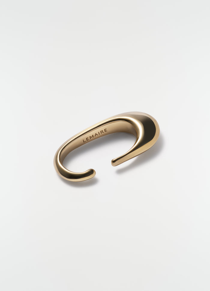 Long drop vermeil gold earcuff by LEMAIRE styled on plain white background close-up detail