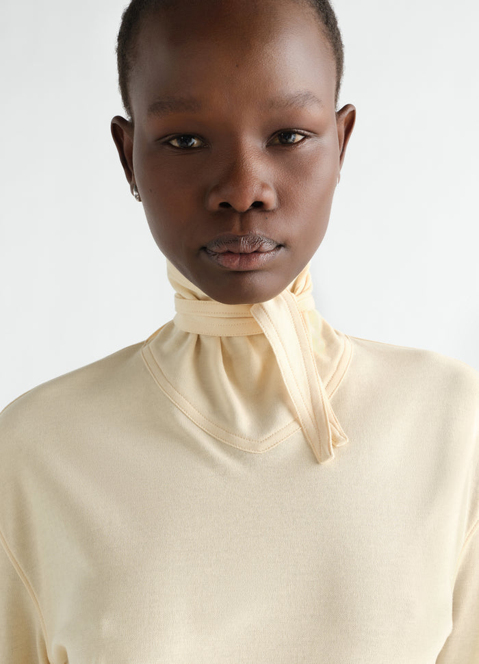 Long-sleeve scarf top in pale yellow silky jersey crepe by LEMAIRE worn by model, close-up front view