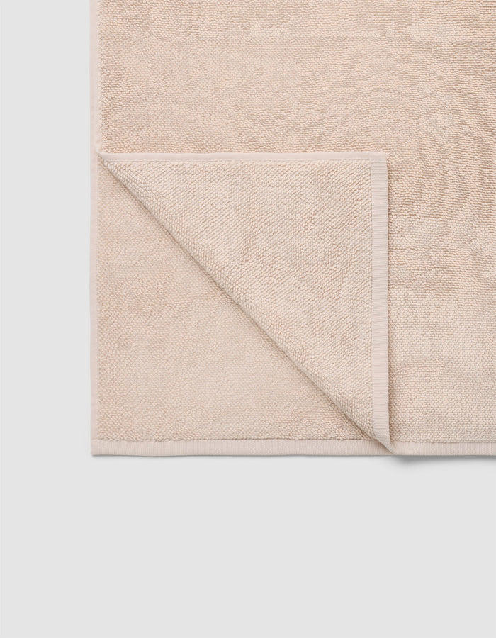 The Cozy Earth Loop Terry Bath Mat is a beige, rectangular mat with one corner folded to reveal its textured underside. Its simple design rests on a light-colored surface.|Color:Petal