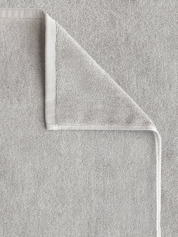 The Cozy Earth Loop Terry Bath Mat, shown in light grey, is neatly folded at one corner to display both sides and its detailed edge stitching. The soft, absorbent texture enhances comfort and style in any bathroom setting.|Color:Light Grey