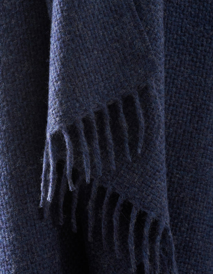 A close-up of the Lucia Throw by Cozy Earth shows its dark blue, textured woven fabric with fringed edges hanging down.|Color:Indigo
