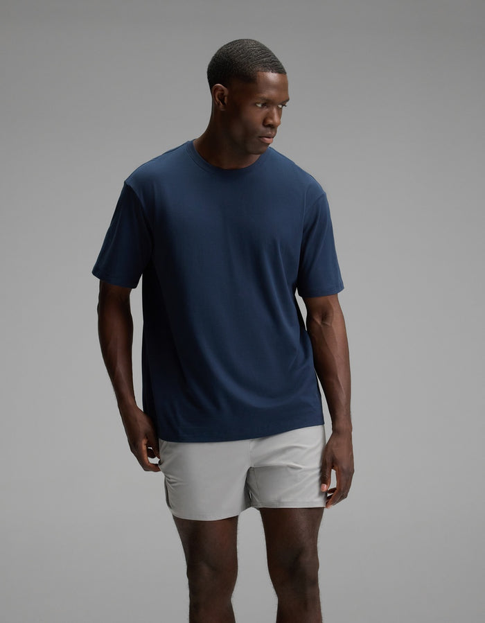A man wearing the Cozy Earth Men’s All Day Tee in Eclipse stands against a plain gray background, looking to his left with a neutral expression.|Color:Eclipse