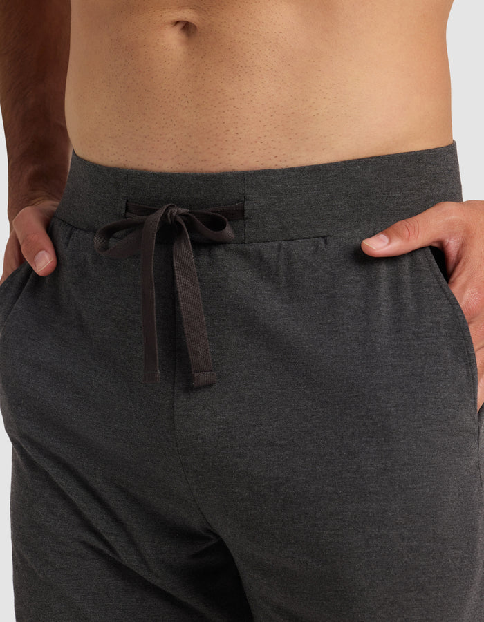 A close-up of a person wearing Cozy Earth's Men's Bamboo Stretch-Knit Pajama Short in dark gray, with hands in the pockets. The shirtless model is shown from waist to upper thighs, highlighting the comfortable stretch-knit fabric.|Color:Charcoal