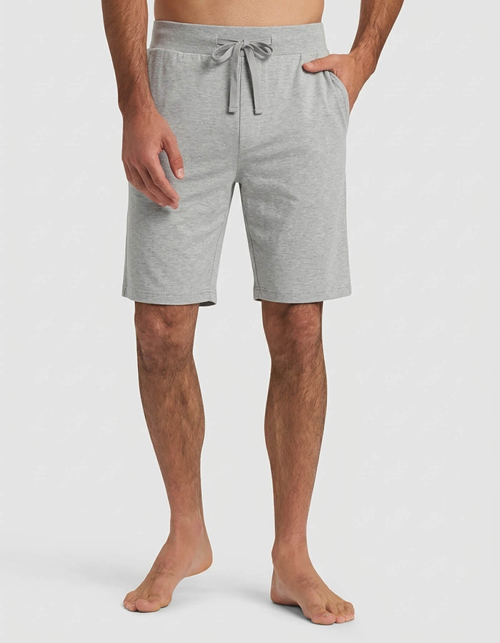 A man wears the Cozy Earth Men's Bamboo Stretch-Knit Short Sleeve Pajama Set in light gray shorts with a drawstring waist and side pockets, standing barefoot against a plain white background.|Color:Heather Grey
