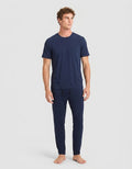 A man stands barefoot against a light gray background, wearing Cozy Earth’s Men's Bamboo Stretch-Knit Lounge Tee & Pant Pajama Set in navy.|Color:Navy