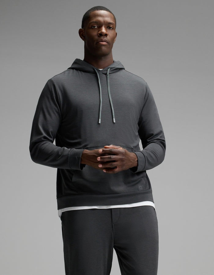 A man stands against a plain gray background wearing the Cozy Earth Men’s Brushed Bamboo Hoodie & Jogger Set, with his hands clasped together in front of him.|Color:Charcoal