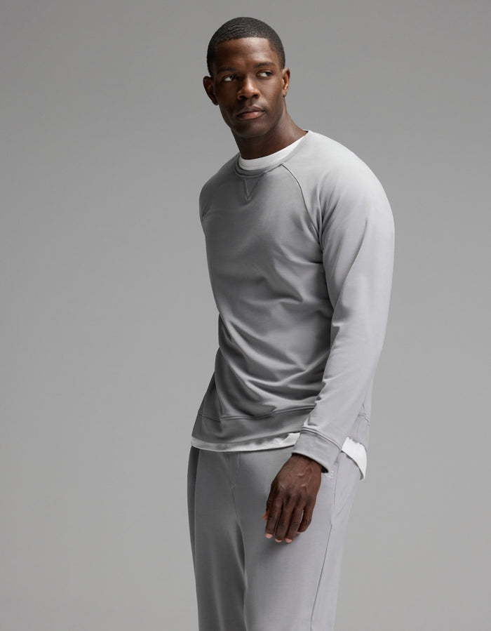A man stands against a plain background, wearing the Cozy Earth Men’s Brushed Bamboo Jogger Set in light gray, with a white shirt peeking out underneath. He looks slightly to his left with a calm expression.|Color:Stone
