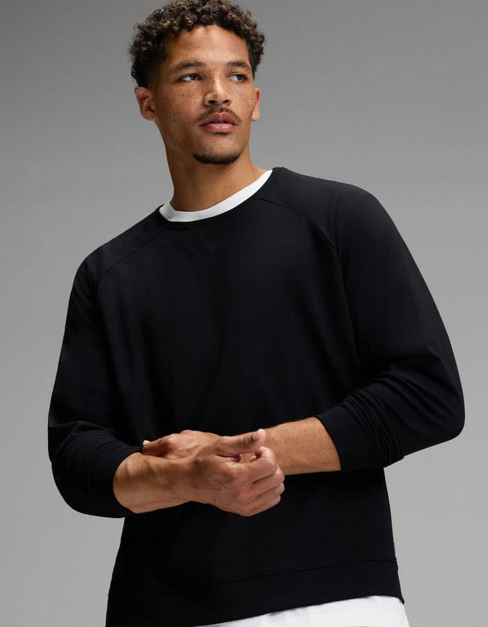 A man with short curly hair and a trimmed beard models the Cozy Earth Men’s Brushed Bamboo Jogger Set in black, layered over a white undershirt, as he stands against a gray background and looks to the side.|Color:Black