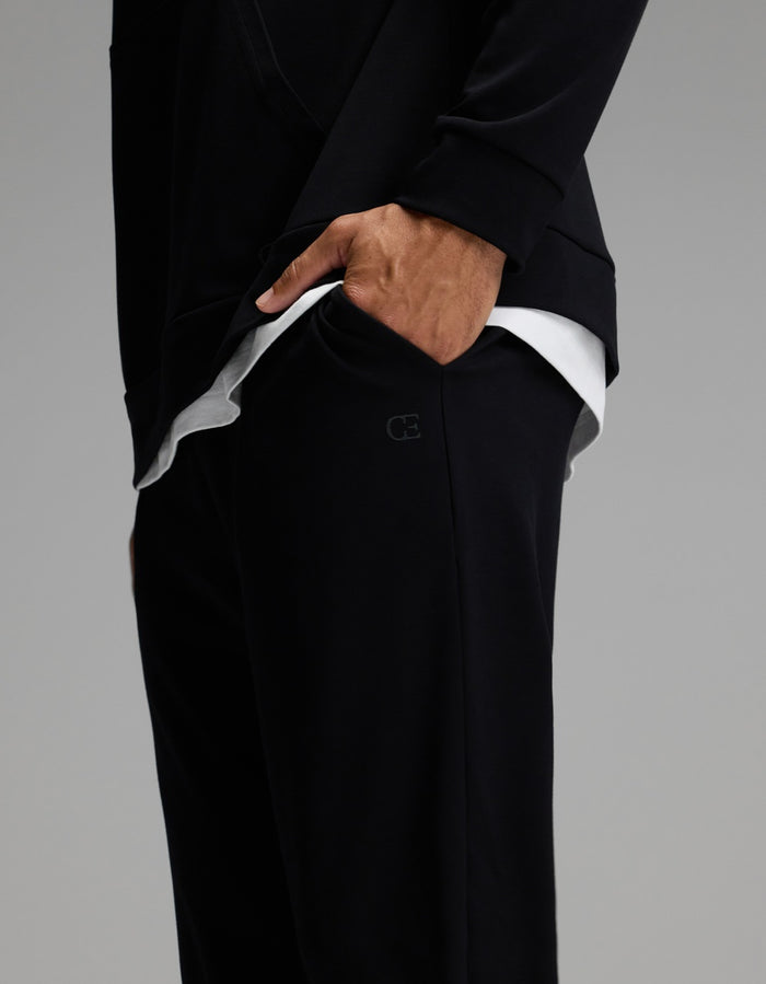 A person wearing Cozy Earth Men’s Brushed Bamboo Joggers paired with a black long-sleeve top, hand in pocket, revealing a layered white shirt underneath.|Color:Black