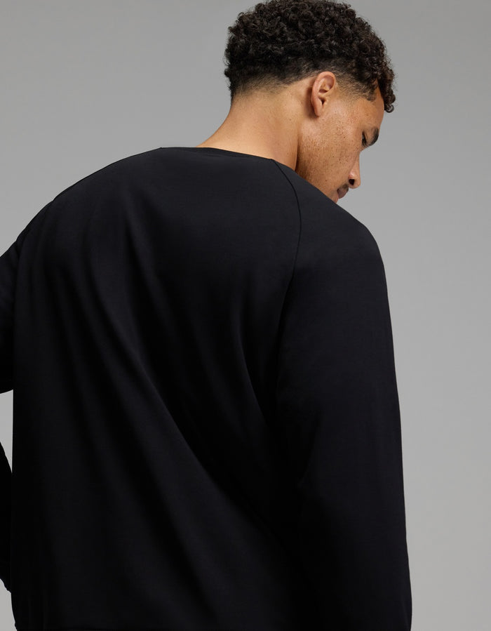 A person with short curly hair is shown from behind, wearing the Cozy Earth Men’s Brushed Bamboo Pullover Crew in plain black, standing against a neutral gray background.|Color:Black