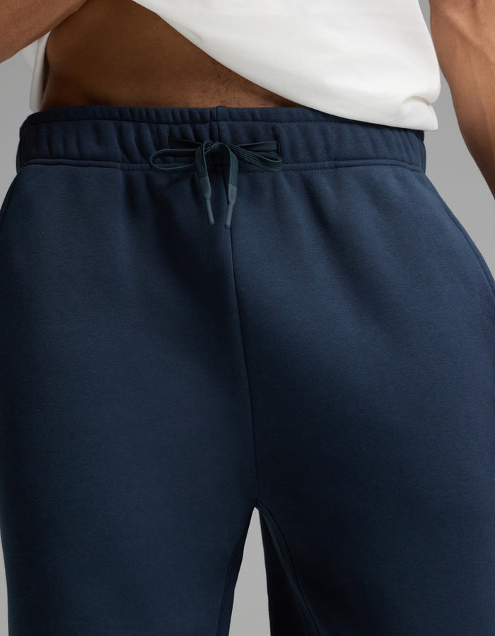 A person wearing a white shirt and Cozy Earth’s Men’s Cityscape Sweatpant in navy blue; the image is cropped to show only the lower torso and upper legs.|Color:Eclipse