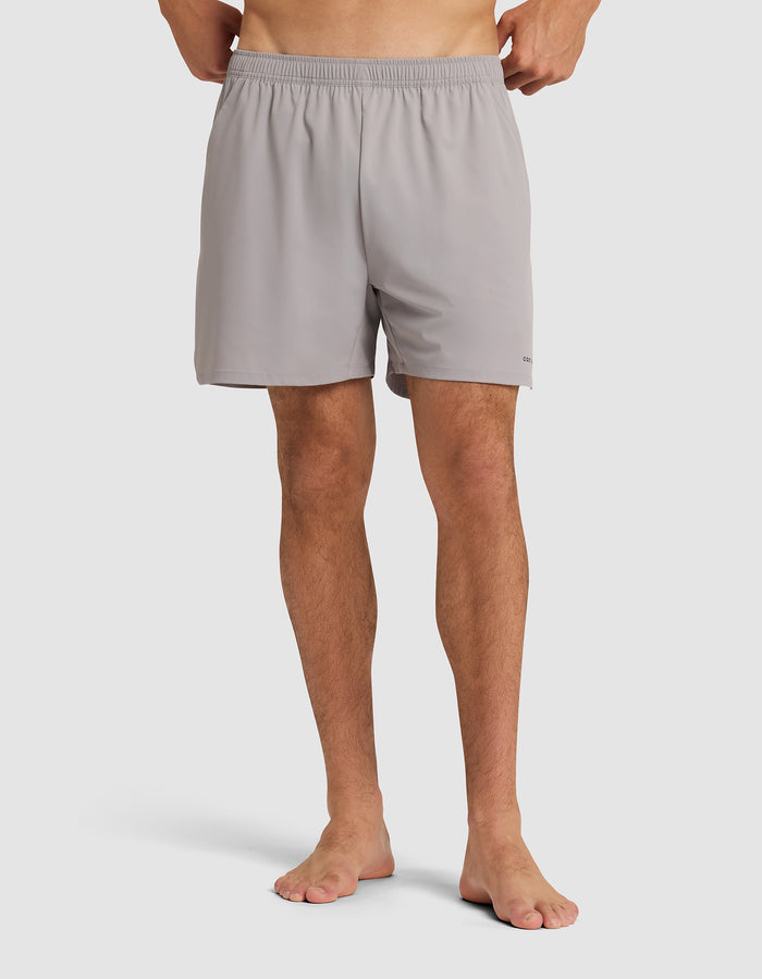 A person stands barefoot wearing the Cozy Earth Men's Day & Night Short 5" in light gray, featuring an elastic waistband. The image is cropped from the waist down against a plain white background. |Color:Stone