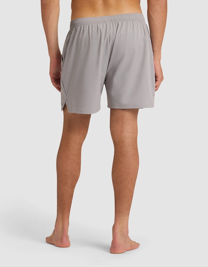 A man stands barefoot, facing away from the camera, wearing Cozy Earth Men's Day & Night Shorts 5" in light gray with an elastic waistband, set against a plain white background. |Color:Stone