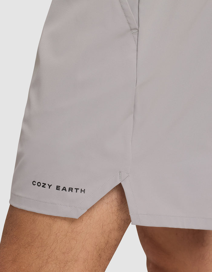 A close-up of a person wearing Cozy Earth Men's Day & Night Shorts 5" in light gray, featuring the brand name near the left hem, a small side slit, and a visible pocket seam. |Color:Stone