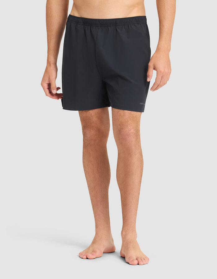 A man stands barefoot against a plain background, wearing Cozy Earth Men's Day & Night Shorts 5" with an elastic waistband. His upper body is not visible in the image. |Color:Jet Black