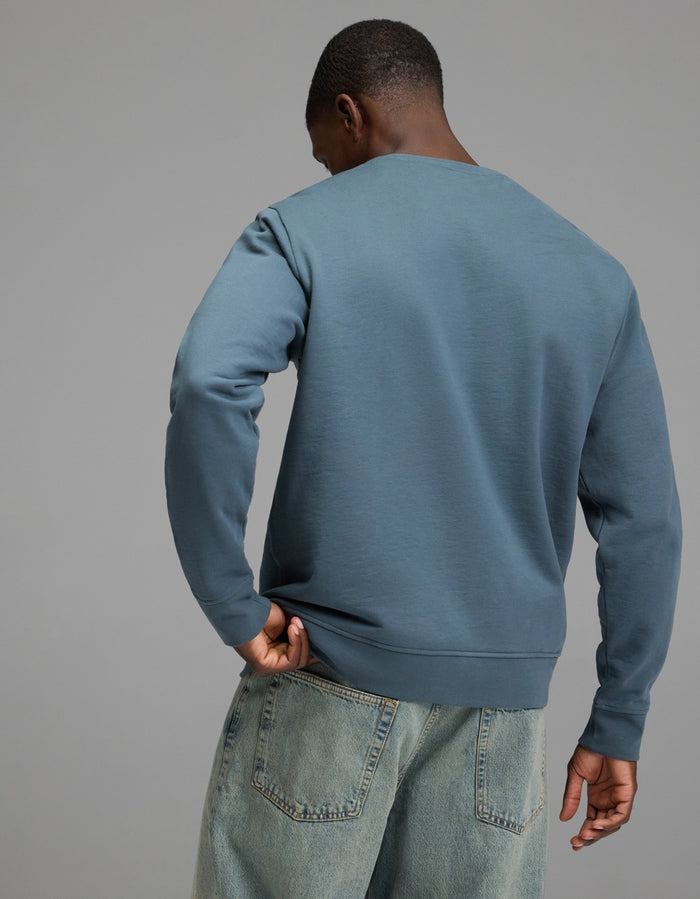 A person wearing the Cozy Earth Men’s Dylan Crewneck and light blue jeans stands with their back to the camera against a plain gray background.|Color:Dawn