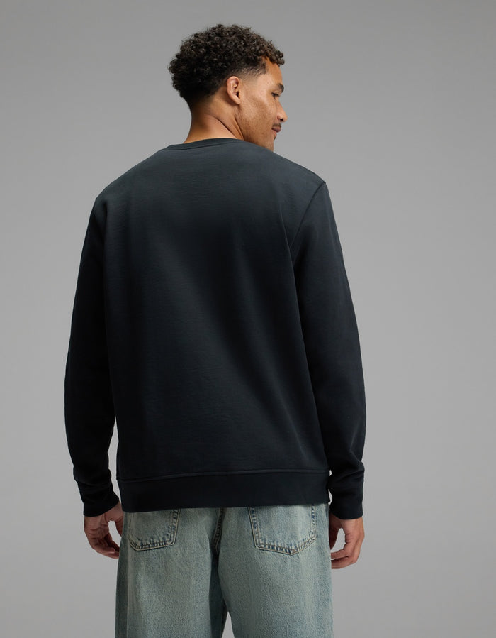 A man stands facing away, wearing the Cozy Earth Men’s Dylan Crewneck in black and light blue jeans, against a plain gray background.|Color:Jet Black