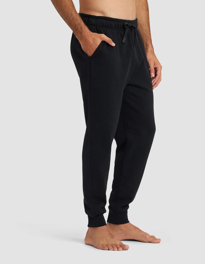 A man stands barefoot wearing Cozy Earth's Men's Dylan Jogger, featuring pockets and a drawstring waist, shown from mid-chest to feet against a plain light gray background.|Color:Jet Black