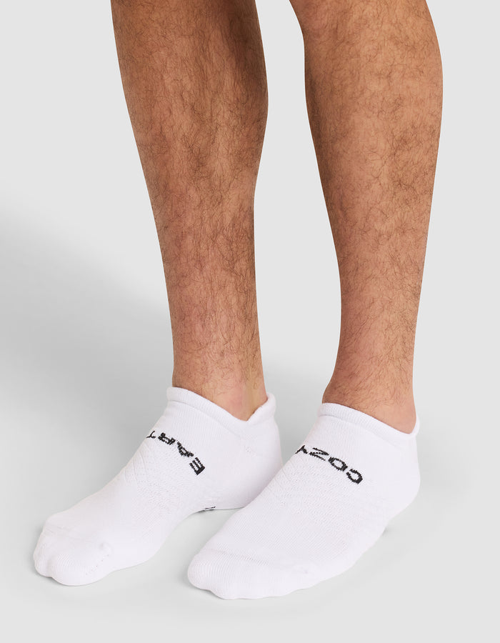 A close-up of a person's lower legs wearing Cozy Earth Essential Ankle Socks in white with black text, standing on a neutral gray background. |Color:White