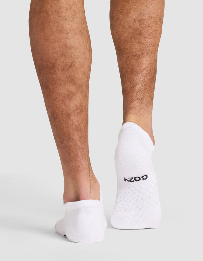 Back view of a person wearing Cozy Earth Essential Ankle Socks in white, which cover the feet up to the ankles. "COZY" is printed in black on the sole. The background is plain and light-colored. |Color:White