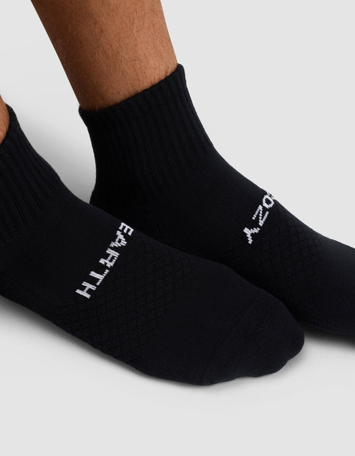 A close-up of two feet wearing Cozy Earth's Essential Quarter Socks in black. "EARTH" is written in white on the left sock and "ZOOM" on the right, set against a light gray background.|Color:Black