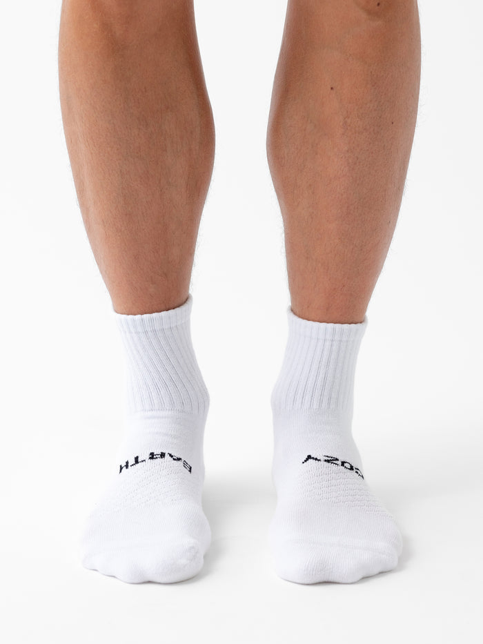 A person wearing Cozy Earth Essential Quarter Sock 8-Pack stands on a white background, with only their lower legs and feet visible. |Color:White