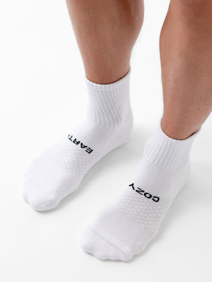 A person wears Cozy Earth Essential Quarter Socks, white with ribbed cuffs. “EARTH” is on the left sock and “COZY” on the right, shown against a plain white background. |Color:White