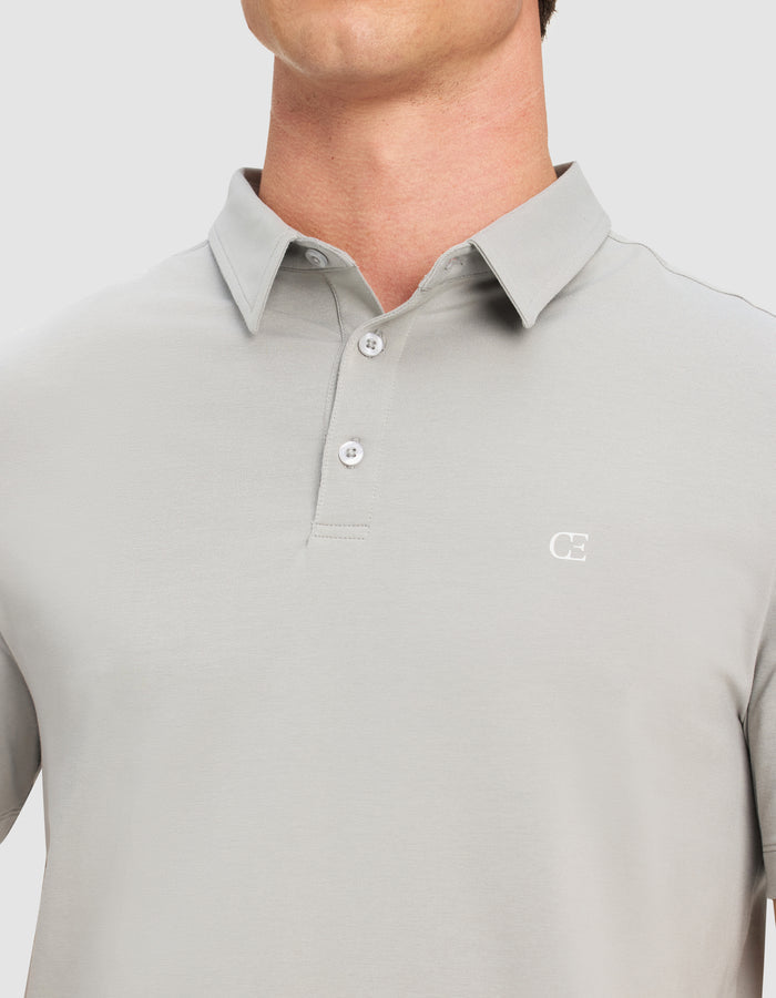 A person wears the Cozy Earth Men's Everyday Polo in light gray, featuring a three-button collar and a small white "CE" logo on the left chest. The image is cropped to show only the shirt and neck.|Color:Stone